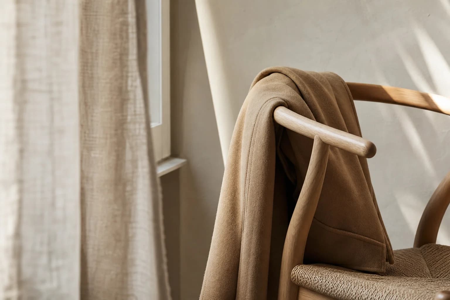 A camel wool coat draped over a pale oak chair in morning light
